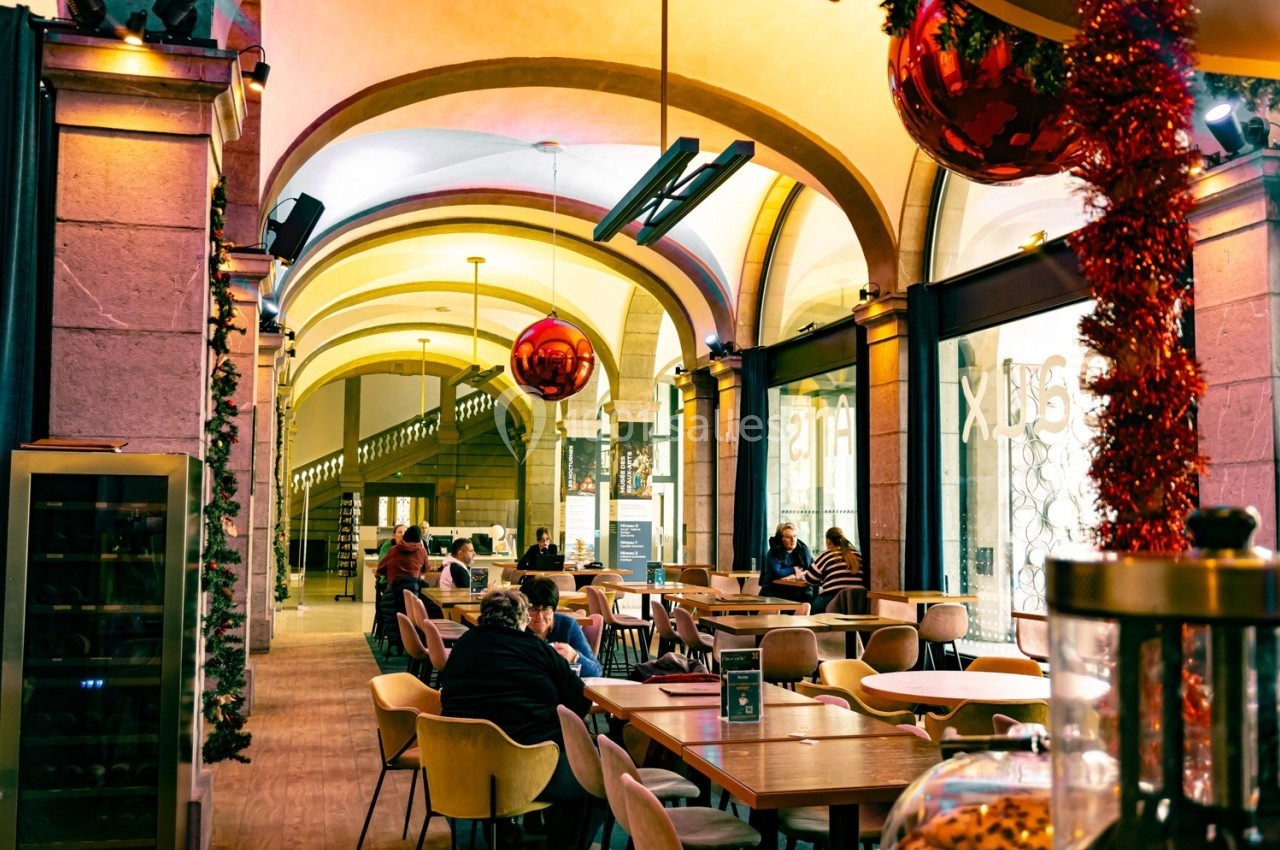 Salle de restaurant lumineuse avec des tables occupées, décorations de Noël suspendues et arches en pierre.