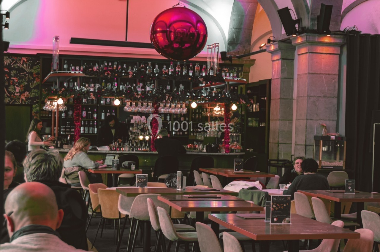 Intérieur d'un bar avec des tables vides, un comptoir garni de bouteilles et un grand ballon rouge suspendu.