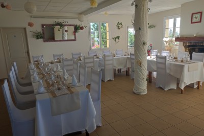 Salle de réception décorée avec des tables rondes dressées, nappes blanches et chaises ornées de nœuds rouges.