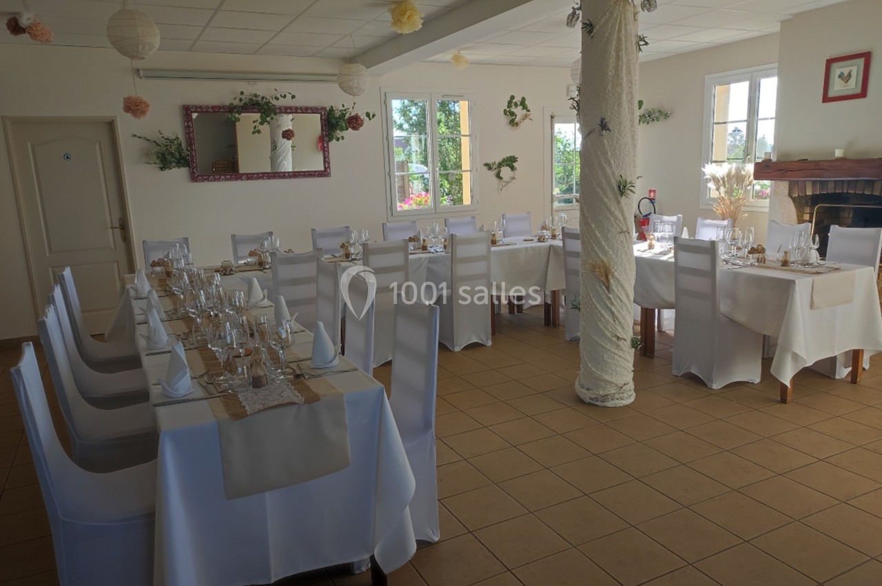 Salle de réception lumineuse avec tables dressées, nappes blanches et décorations florales.