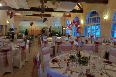 Salle de réception décorée avec des tables rondes dressées, nappes blanches et chaises ornées de nœuds rouges.