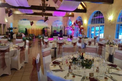Salle de réception décorée avec des tables rondes dressées, nappes blanches et chaises ornées de nœuds rouges.
