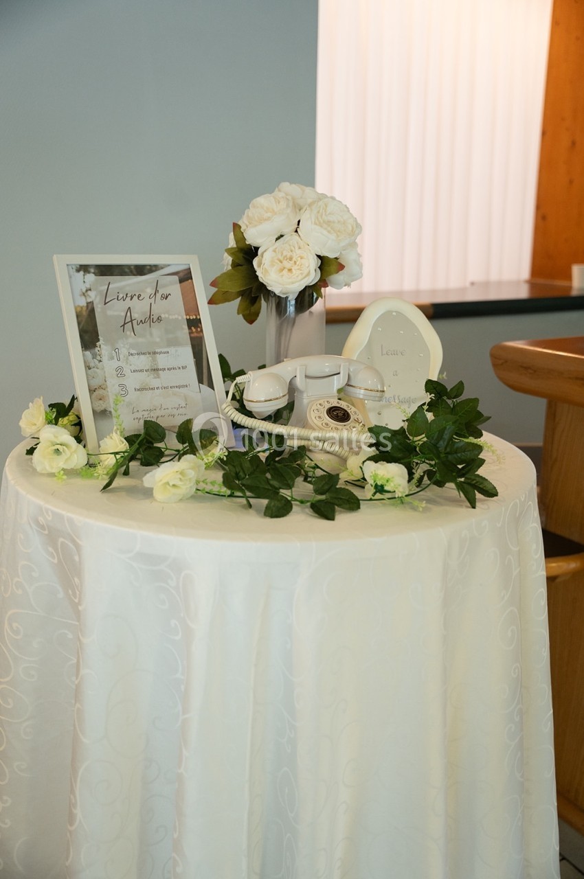 Table ronde décorée avec une nappe blanche, des roses blanches, un livre d'or et un téléphone rétro.
