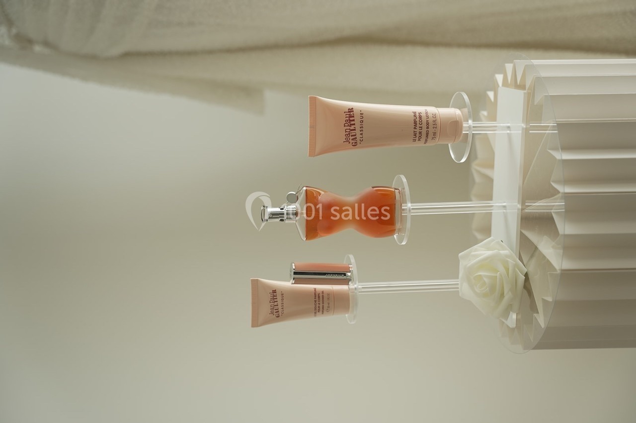 Trois produits cosmétiques sur des supports transparents, posés sur une surface blanche avec une rose décorative.