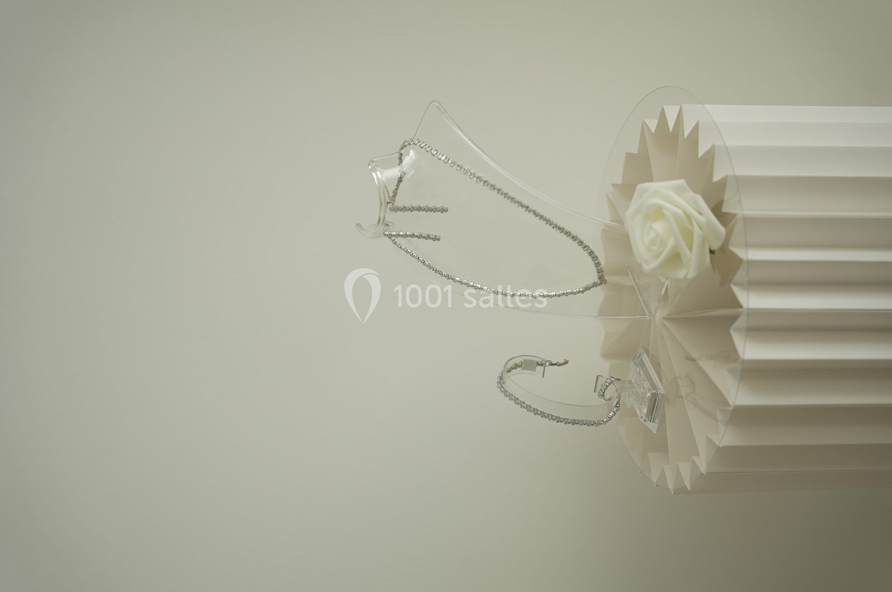 Chaîne en argent posée sur un support cylindrique blanc avec une rose blanche en décoration.