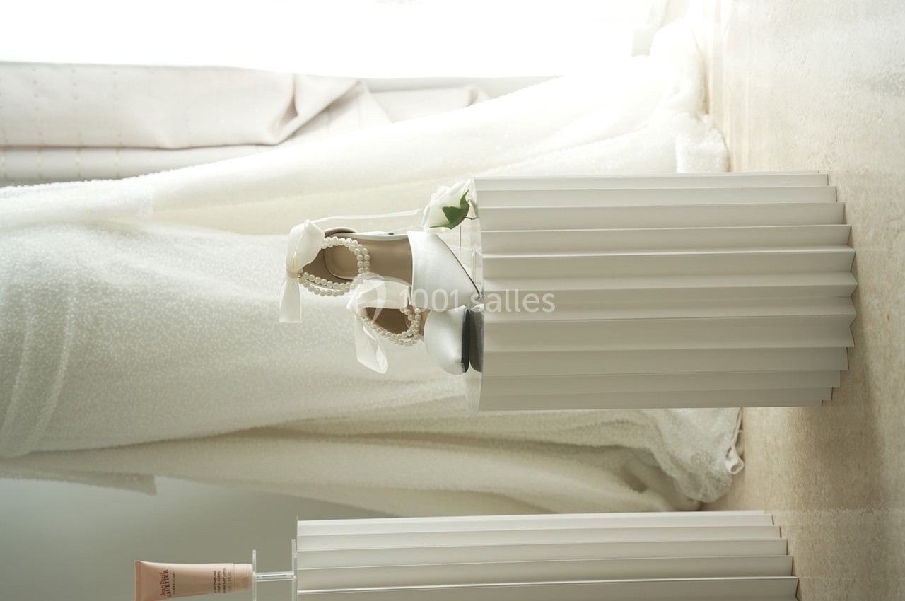 Chaussures blanches ornées de perles et rubans, posées sur un socle plissé dans un intérieur lumineux.