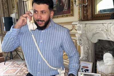 Un homme en chemise rayée bleue utilise un téléphone fixe dans une pièce ornée de décorations classiques.