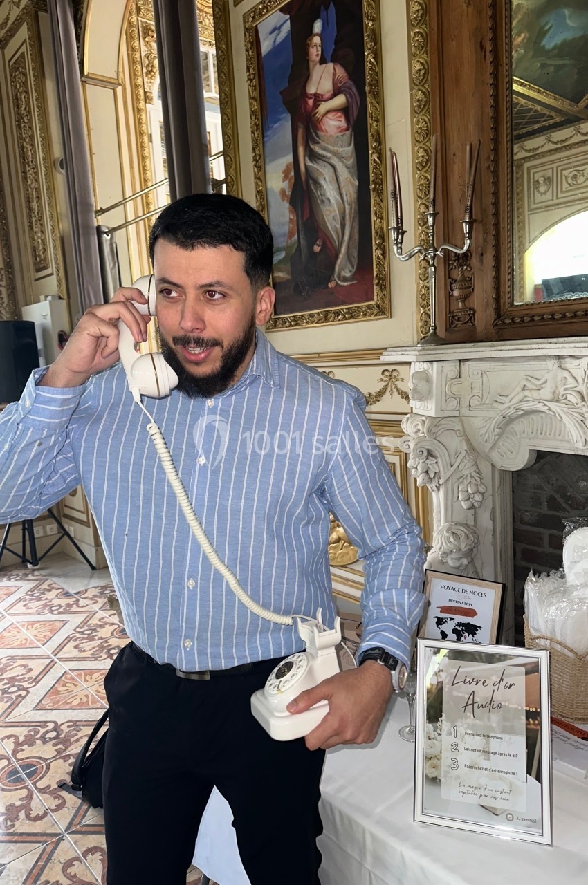 Un homme en chemise rayée bleue utilise un téléphone fixe dans une pièce ornée de décorations classiques.