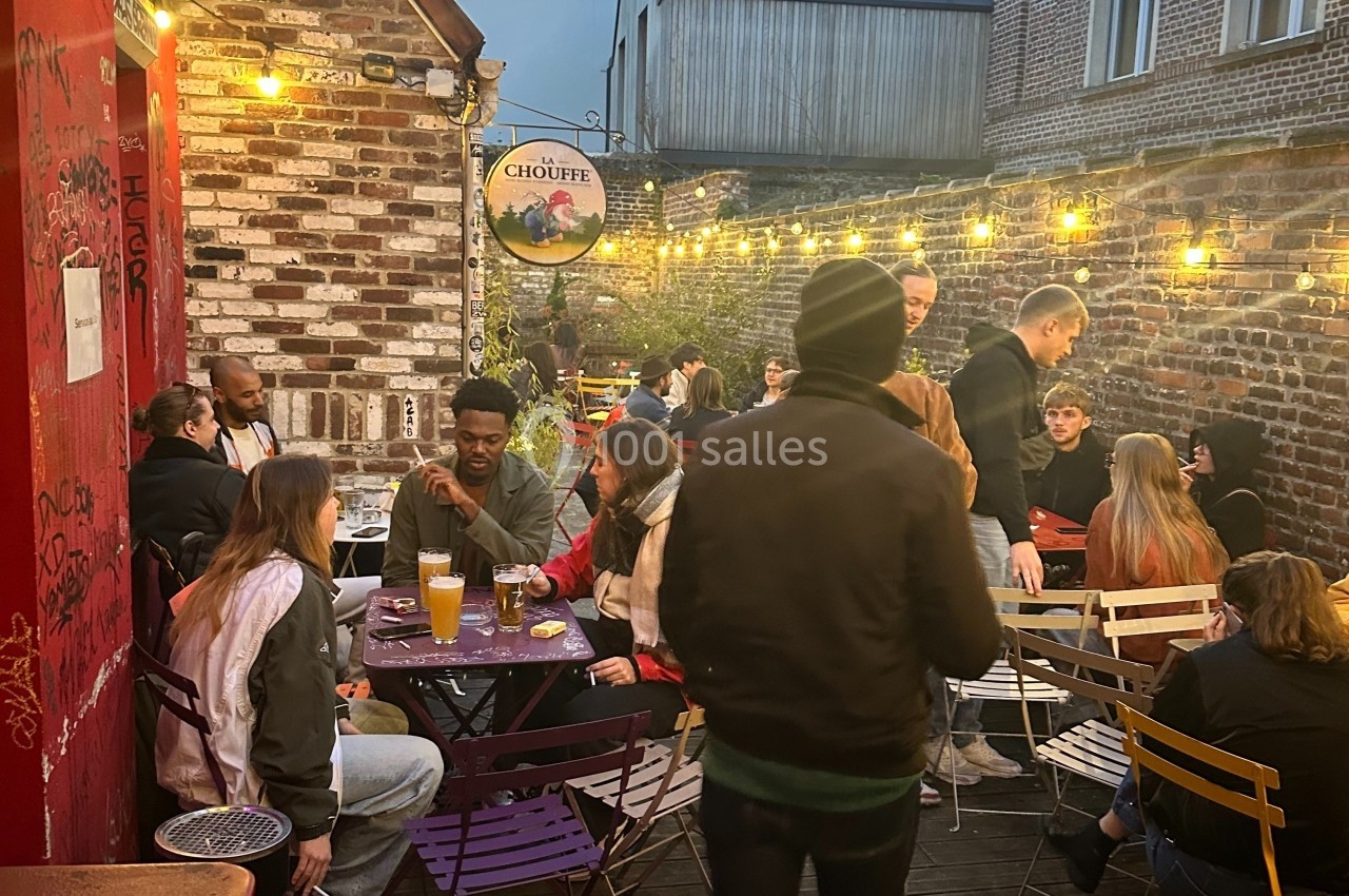 Groupe de personnes discutant et partageant des boissons en terrasse éclairée par des guirlandes lumineuses, ambiance…