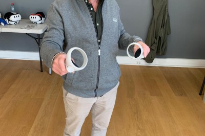 Homme portant un casque de réalité virtuelle et tenant deux manettes dans une pièce au sol en bois.