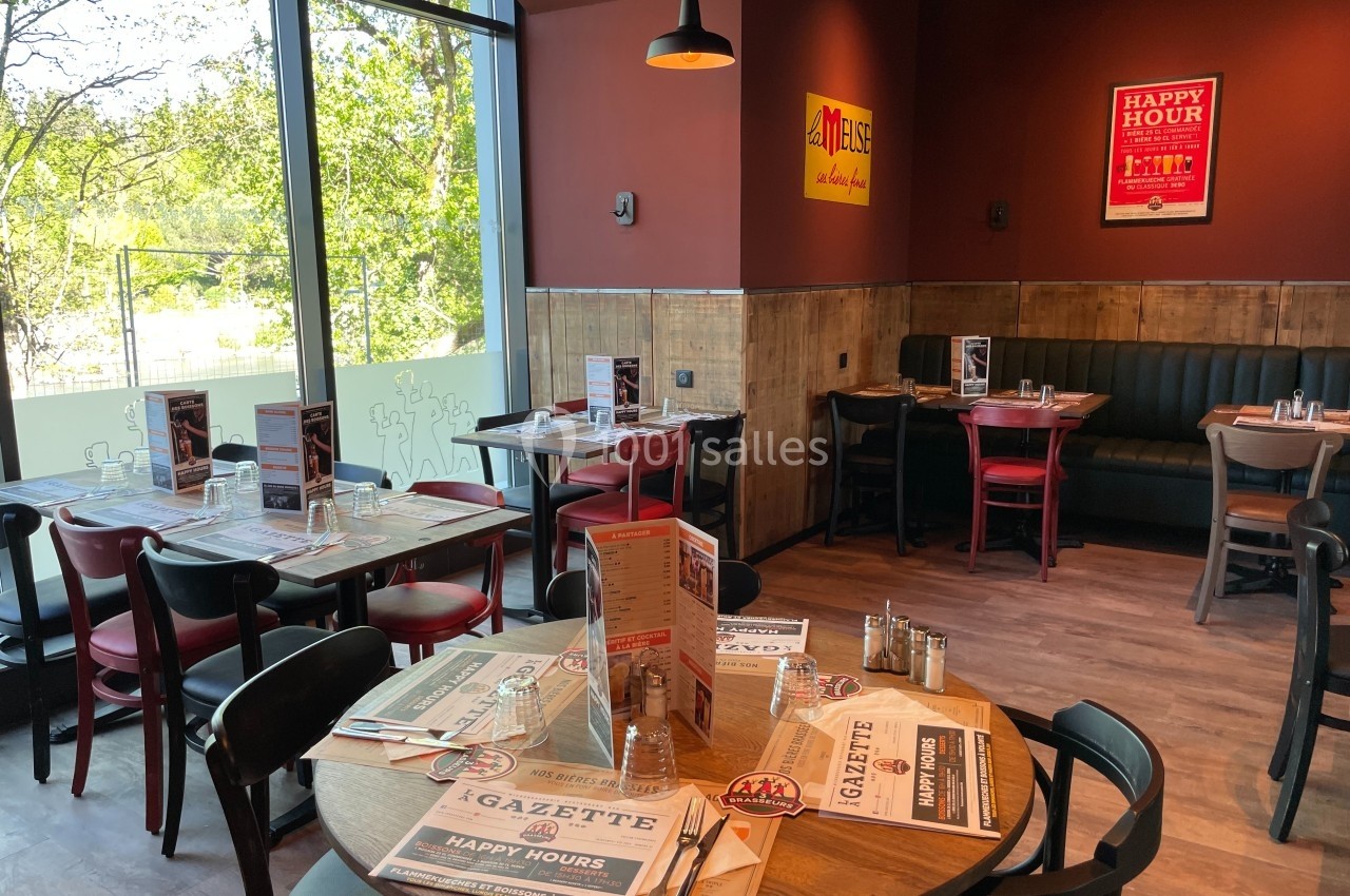 Salle de restaurant avec tables dressées, chaises en bois, banquettes noires et affiches décoratives sur les murs.