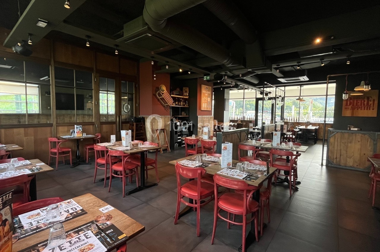 Salle de restaurant avec tables en bois, chaises rouges, menus posés et ambiance chaleureuse grâce à un éclairage tamisé.