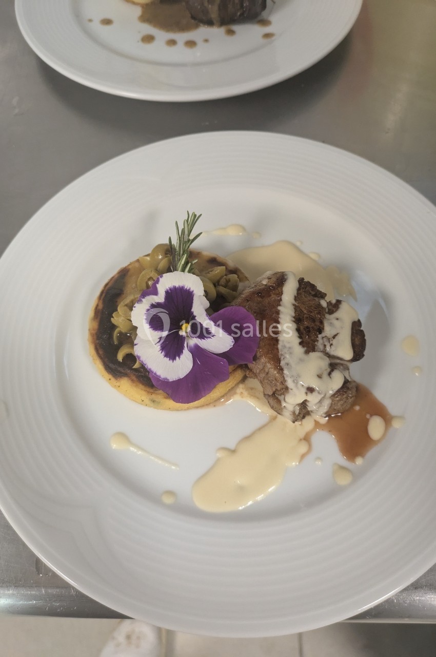 Assiette gastronomique avec viande, purée, sauce crémeuse, champignons et décoration florale comestible.
