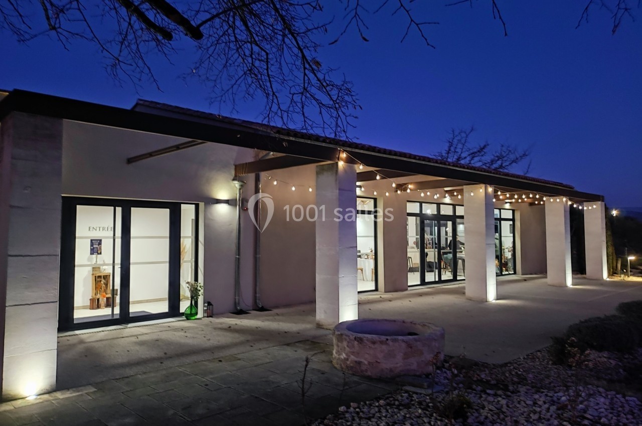Façade d'un bâtiment moderne éclairé de nuit, avec guirlandes lumineuses et terrasse en pierre.