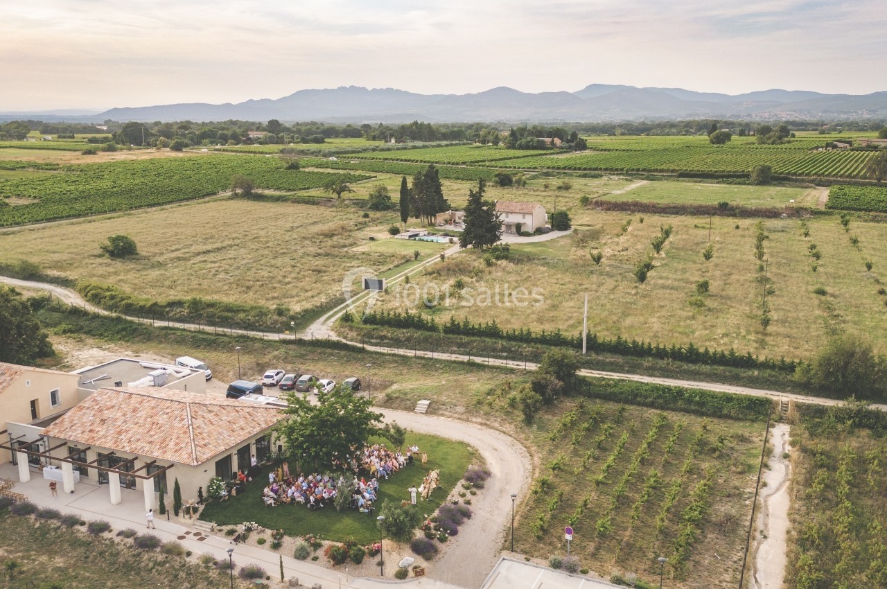 Vue aérienne d'un domaine rural avec vignes, bâtiments et un rassemblement de personnes sur une pelouse.