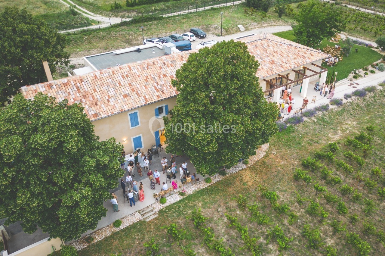 Vue aérienne d'une grande bâtisse avec toit en tuiles, entourée de verdure et de vignes, accueillant un rassemblement.