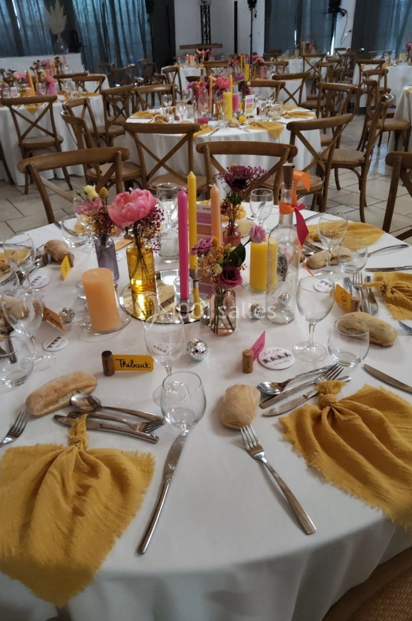 Table de réception décorée avec des nappes blanches, serviettes jaunes, bougies colorées et fleurs au centre.