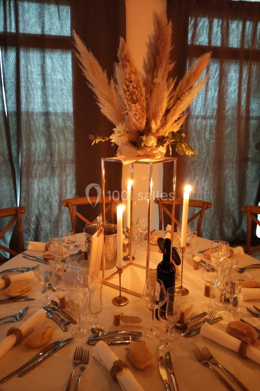 Table dressée pour un dîner avec bougies allumées, décoration florale centrale et couverts disposés autour.