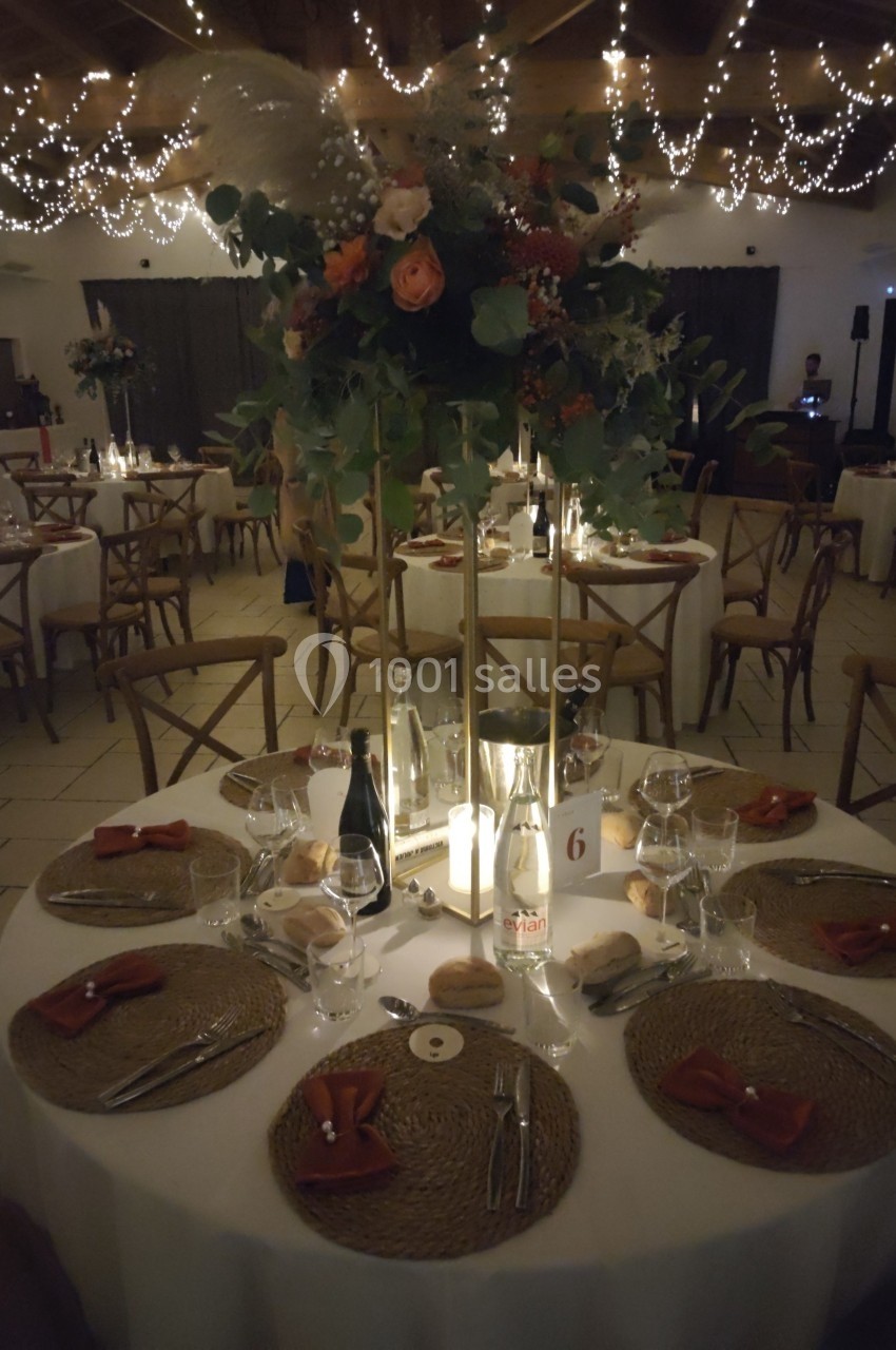 Salle de réception décorée avec des guirlandes lumineuses, tables dressées avec centre de table floral et ambiance tamisée.