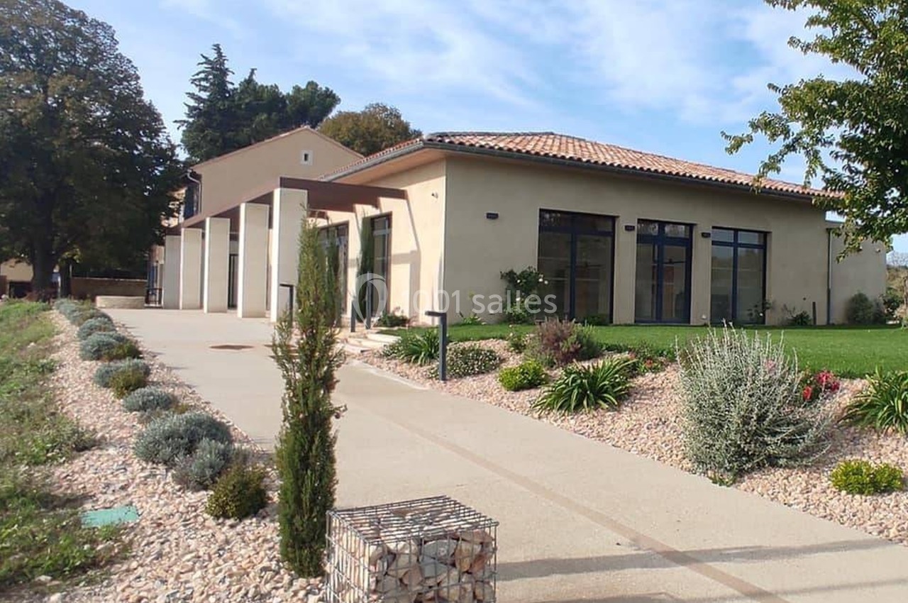 Bâtiment moderne avec toit en tuiles, grandes baies vitrées, allée bordée de plantes et jardin paysager.