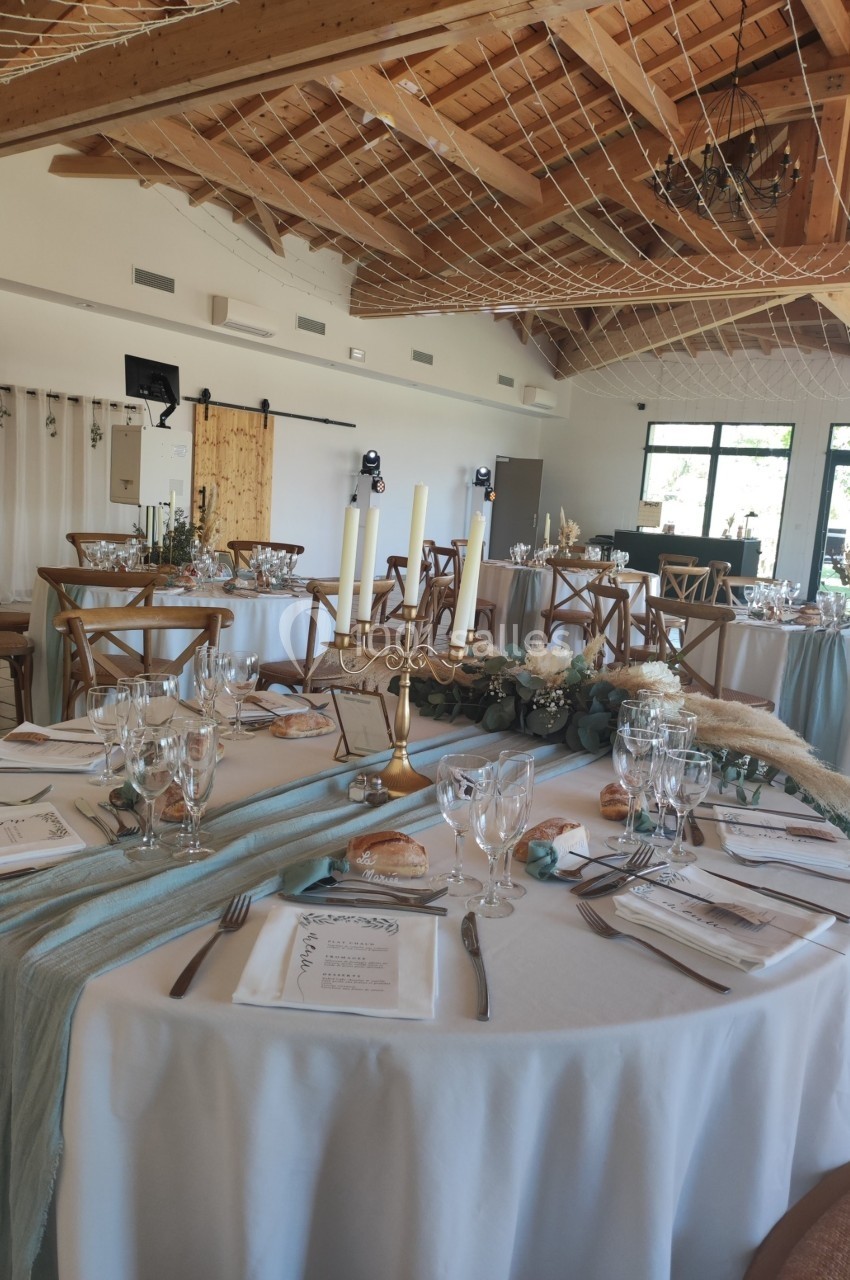 Salle de réception décorée pour un mariage, avec tables rondes dressées, nappes blanches et détails élégants.