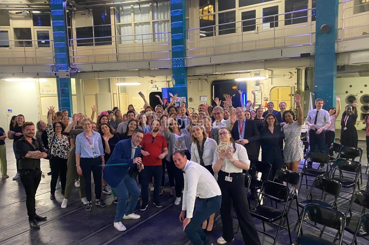 Un groupe de personnes posant ensemble dans une grande salle éclairée, entourée de structures métalliques.