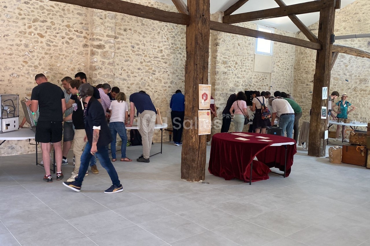Des visiteurs observent des objets exposés sur des tables dans une salle en pierre avec poutres apparentes.