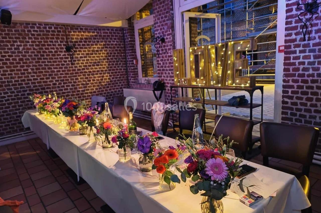 Table décorée avec des fleurs colorées dans une salle en briques, éclairée par des lettres lumineuses formant ’LOVE’.
