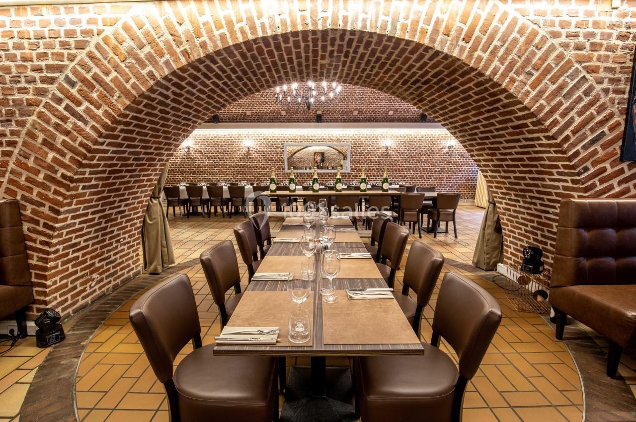 Salle de restaurant voûtée avec murs en briques, tables dressées et chaises en cuir marron.