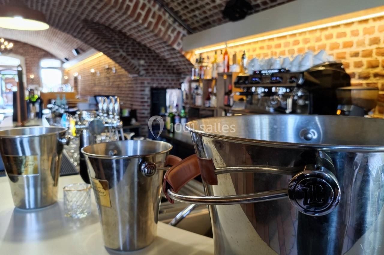 Seaux à champagne en métal disposés sur un comptoir dans un bar à l'intérieur d'une salle voûtée en briques.