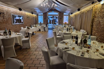 Espace extérieur aménagé pour un événement avec tables hautes, buffet et tente blanche, entouré de verdure.