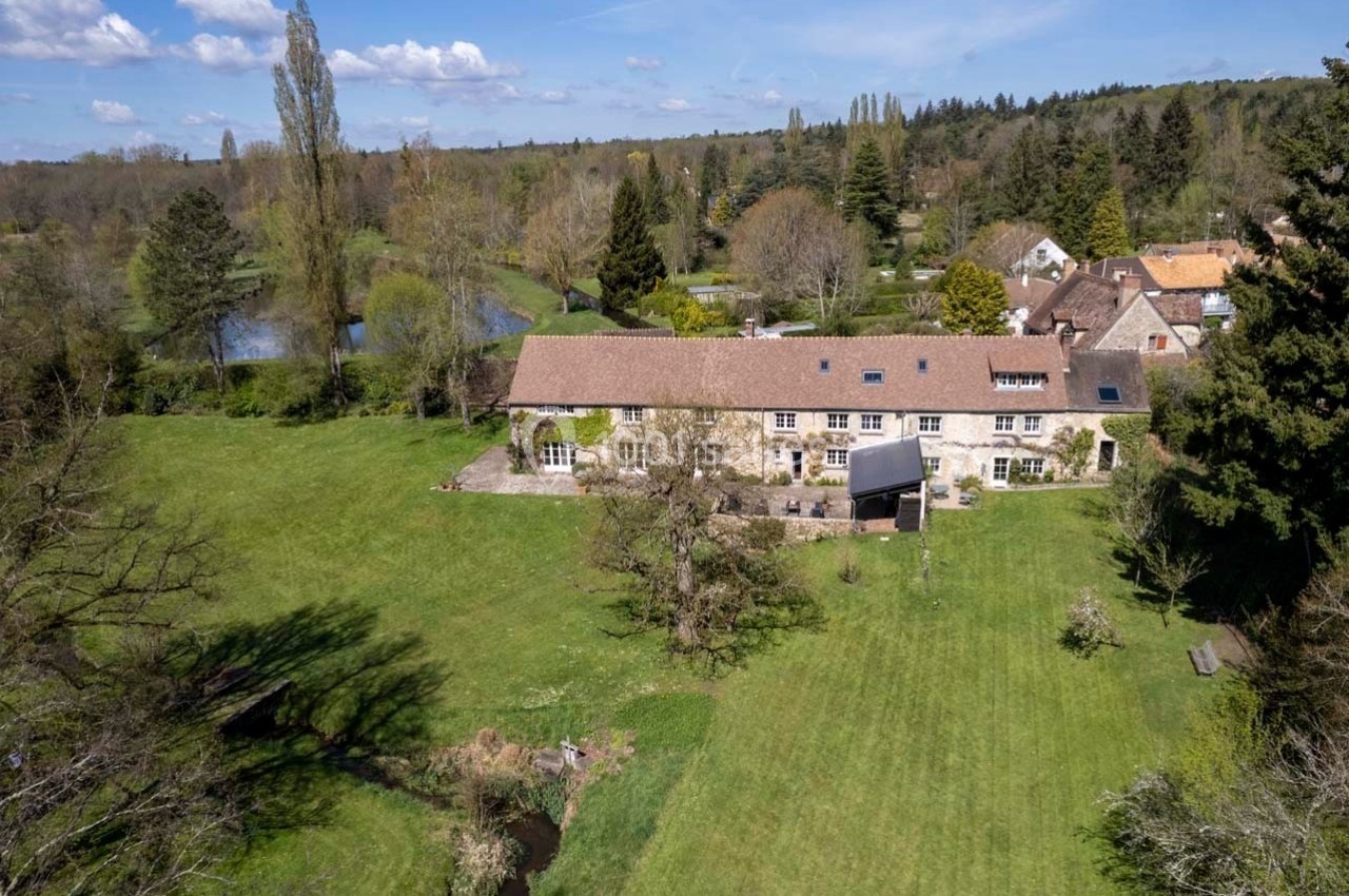 Vue aérienne d'une grande maison en pierre entourée d'un vaste jardin verdoyant et d'arbres, en pleine campagne.
