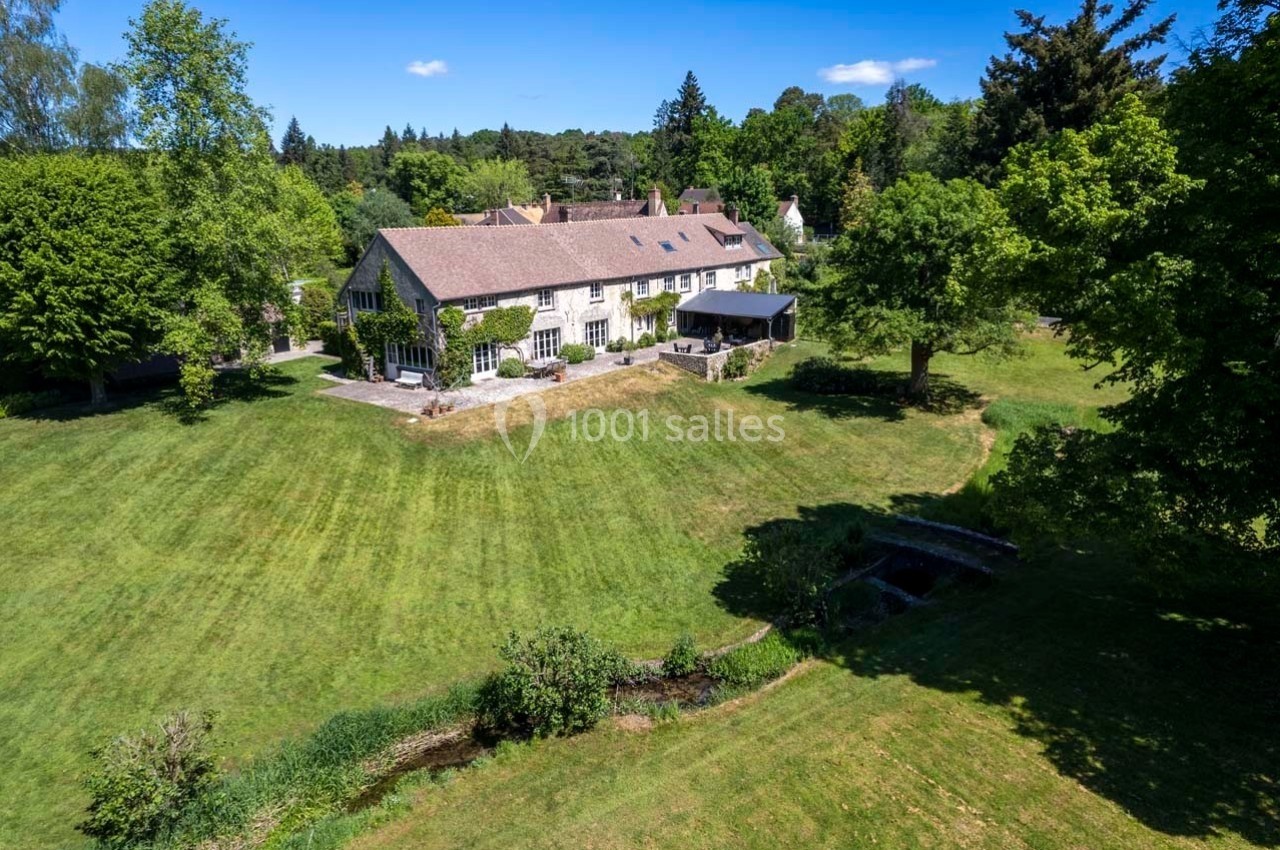 Vue aérienne d'une grande maison en pierre entourée d'un vaste jardin verdoyant avec arbres et pelouse.