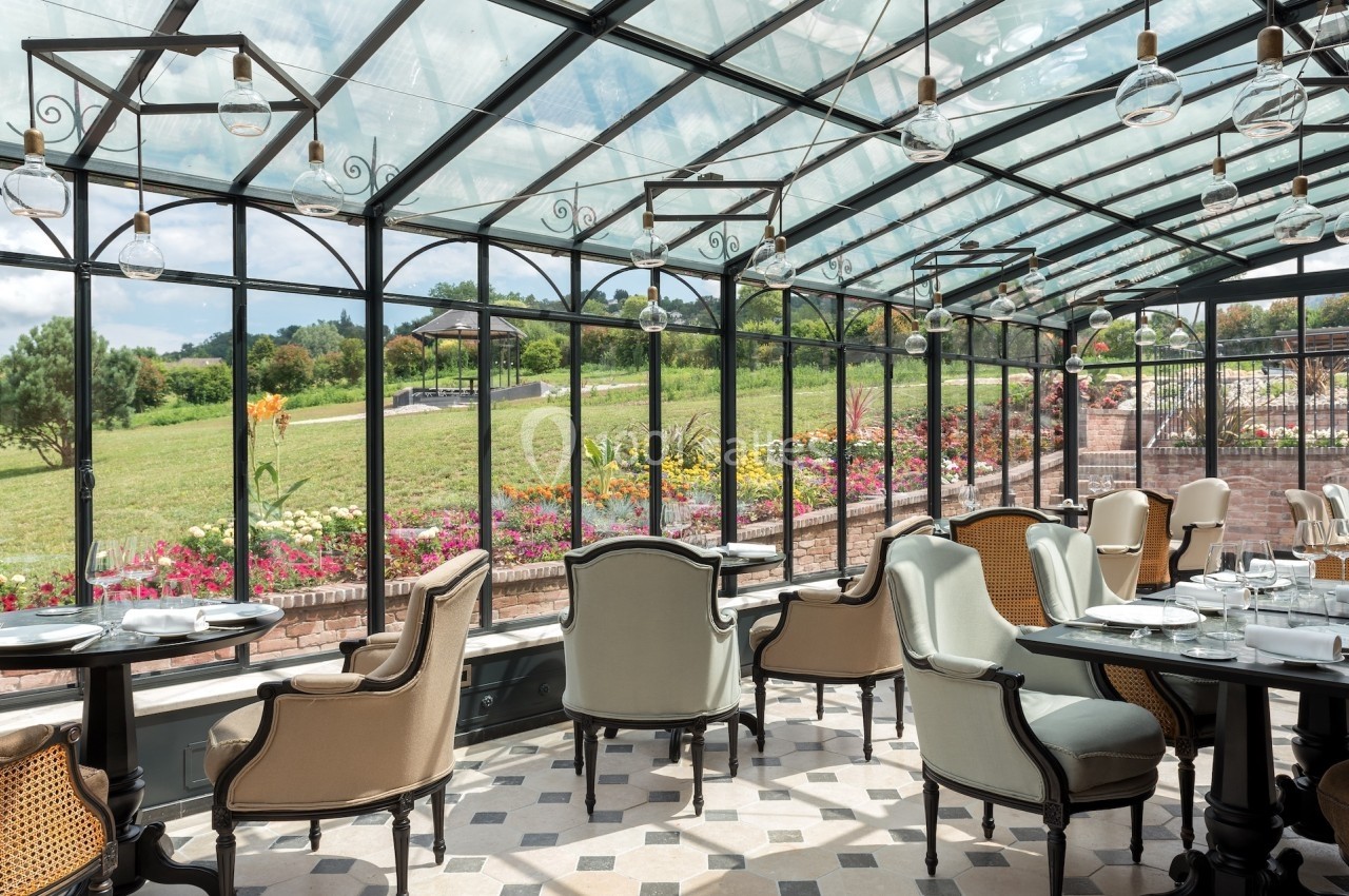 Salle lumineuse avec verrière, mobilier élégant et vue sur un jardin fleuri et un paysage verdoyant.