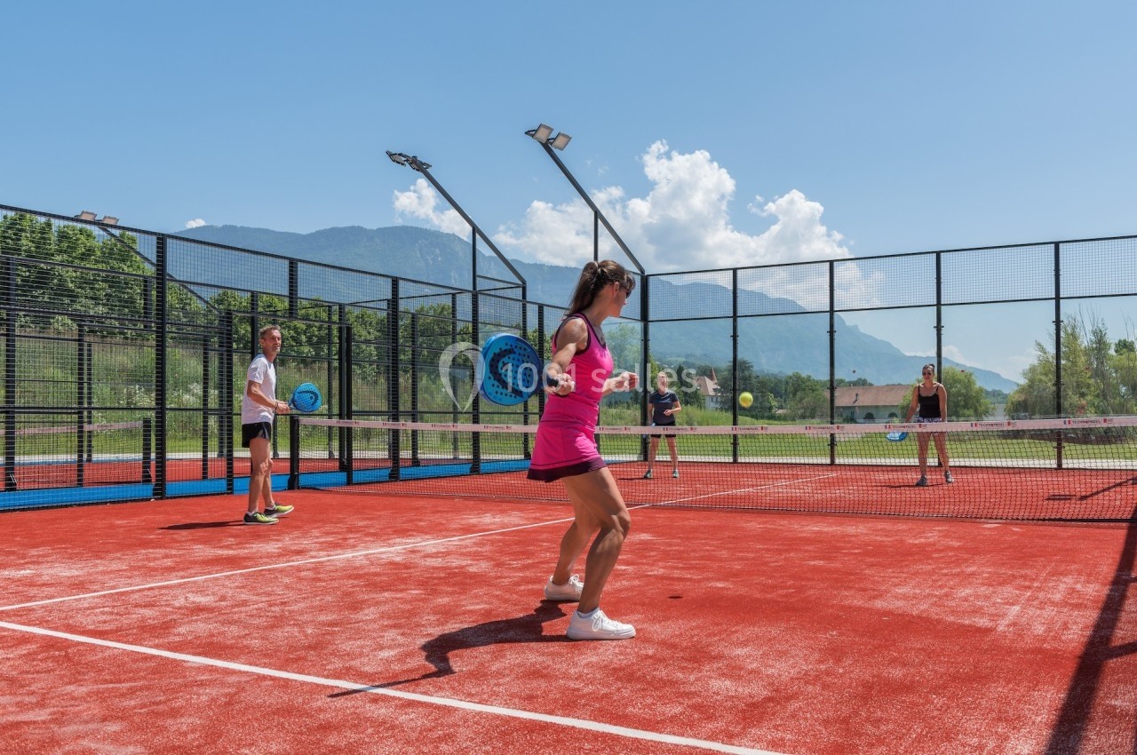 Quatre personnes jouent au padel sur un court extérieur avec vue sur des montagnes et un ciel dégagé.