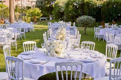 Coussin brodé ’Villa Alexandra’ au premier plan, banc en bois flou en arrière-plan dans un jardin ensoleillé.