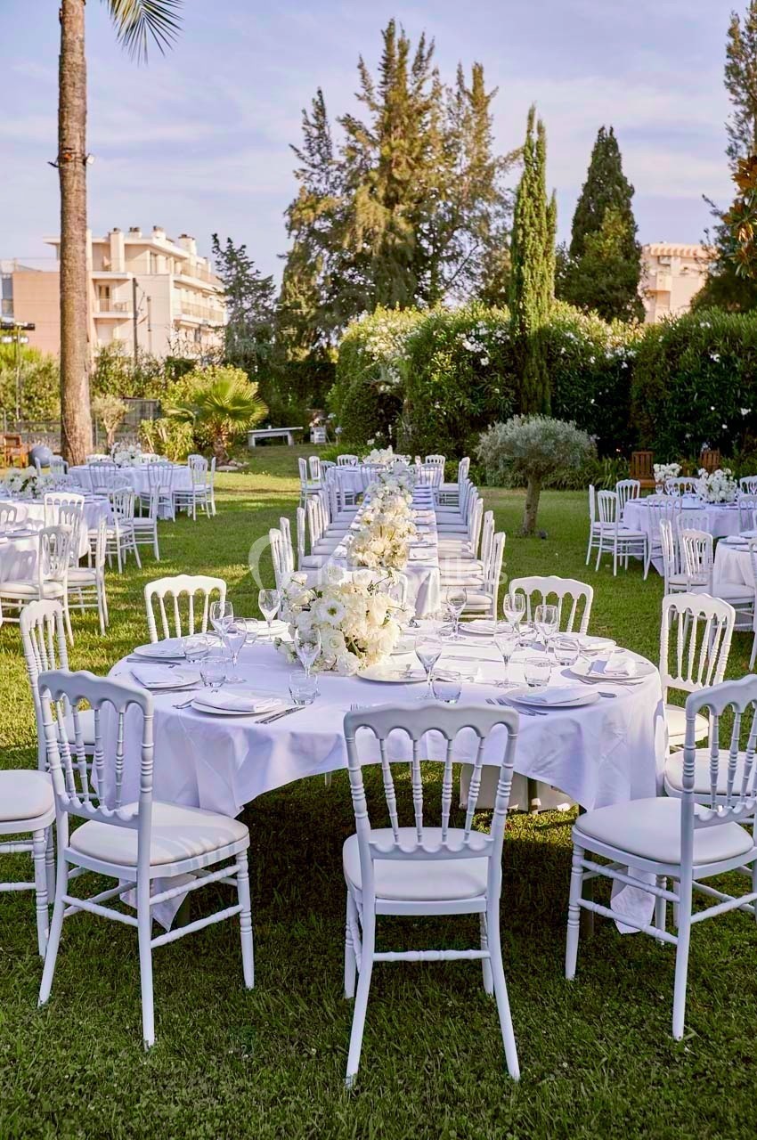 Tables rondes et rectangulaires décorées de nappes blanches et fleurs, disposées dans un jardin pour un événement en plein…