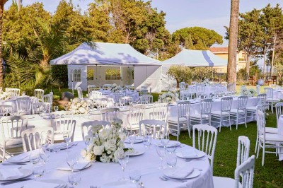 Coussin brodé ’Villa Alexandra’ au premier plan, banc en bois flou en arrière-plan dans un jardin ensoleillé.