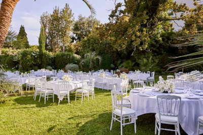 Coussin brodé ’Villa Alexandra’ au premier plan, banc en bois flou en arrière-plan dans un jardin ensoleillé.