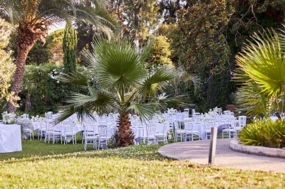 Coussin brodé ’Villa Alexandra’ au premier plan, banc en bois flou en arrière-plan dans un jardin ensoleillé.