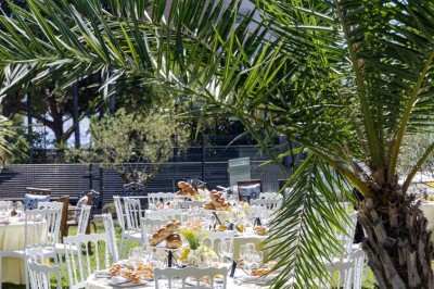 Coussin brodé ’Villa Alexandra’ au premier plan, banc en bois flou en arrière-plan dans un jardin ensoleillé.