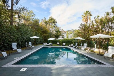 Coussin brodé ’Villa Alexandra’ au premier plan, banc en bois flou en arrière-plan dans un jardin ensoleillé.