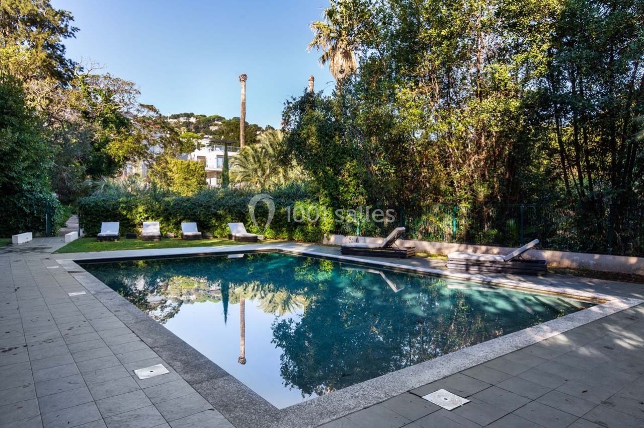 Piscine extérieure entourée de végétation luxuriante, avec des transats alignés sur une terrasse carrelée.
