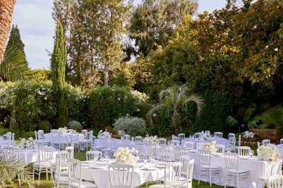 Deux fauteuils en rotin et une table basse avec une tasse, sur une terrasse donnant sur un jardin verdoyant.