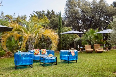 Deux fauteuils en rotin et une table basse avec une tasse, sur une terrasse donnant sur un jardin verdoyant.