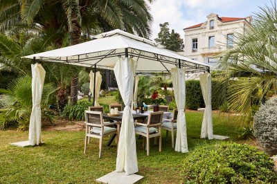 Deux fauteuils en rotin et une table basse avec une tasse, sur une terrasse donnant sur un jardin verdoyant.