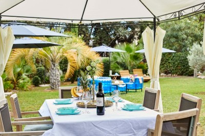 Deux fauteuils en rotin et une table basse avec une tasse, sur une terrasse donnant sur un jardin verdoyant.