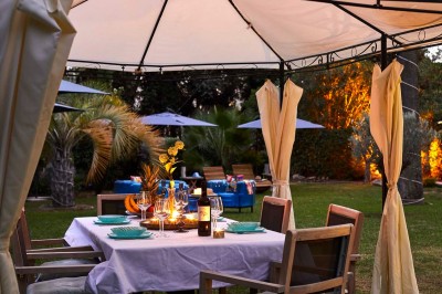 Deux fauteuils en rotin et une table basse avec une tasse, sur une terrasse donnant sur un jardin verdoyant.
