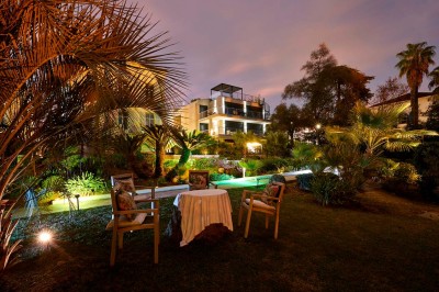 Deux fauteuils en rotin et une table basse avec une tasse, sur une terrasse donnant sur un jardin verdoyant.