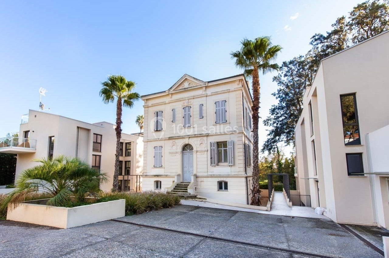 Façade d'un bâtiment ancien entouré de palmiers, avec des constructions modernes à proximité.